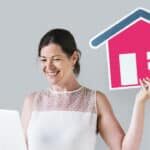 Woman holding a house icon and using a laptop